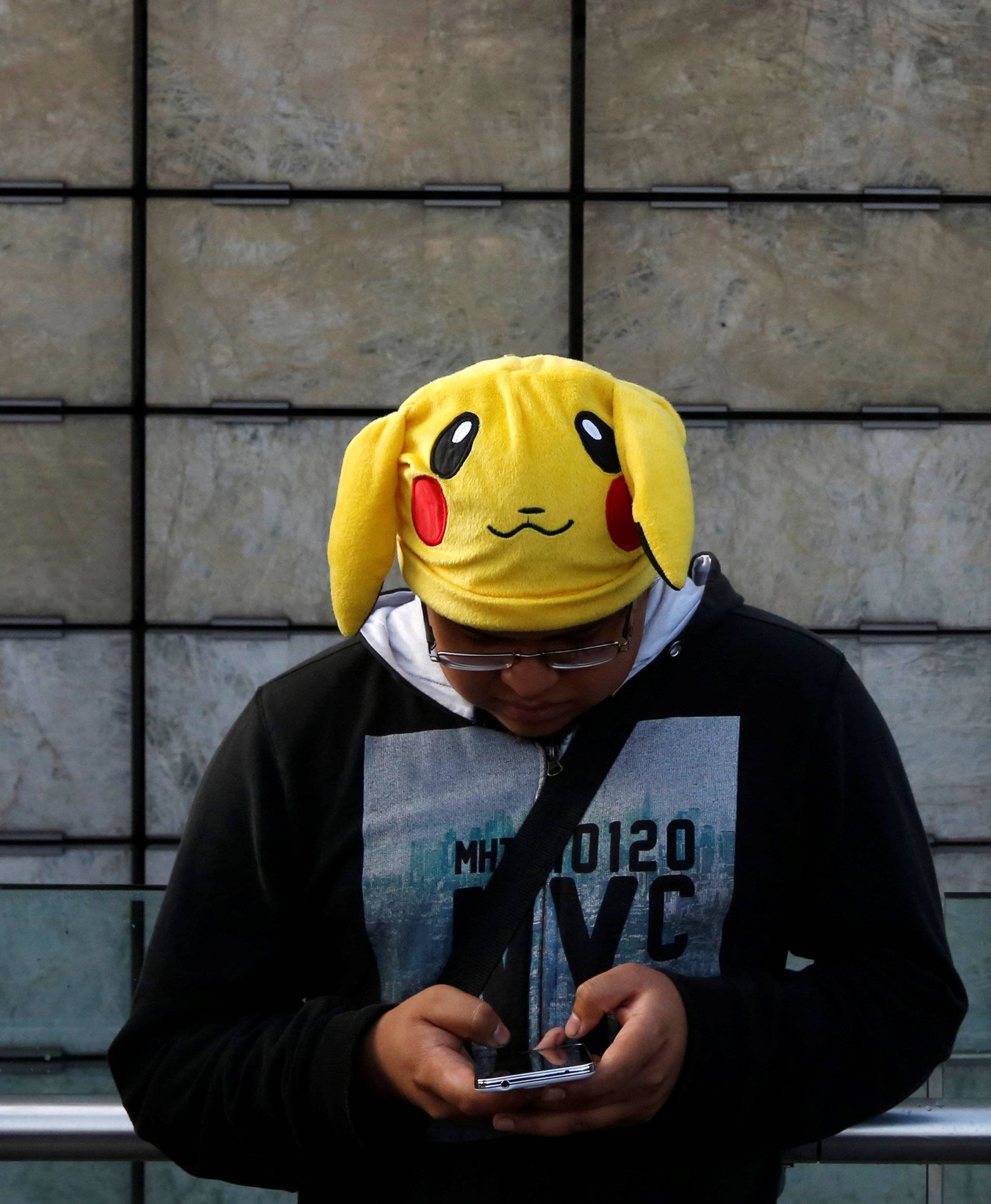A man wearing a Pikachu hat, a character from Pokemon, plays Pokemon Go during a gathering to celebrate "Pokemon Day" in Mexico City, Mexico