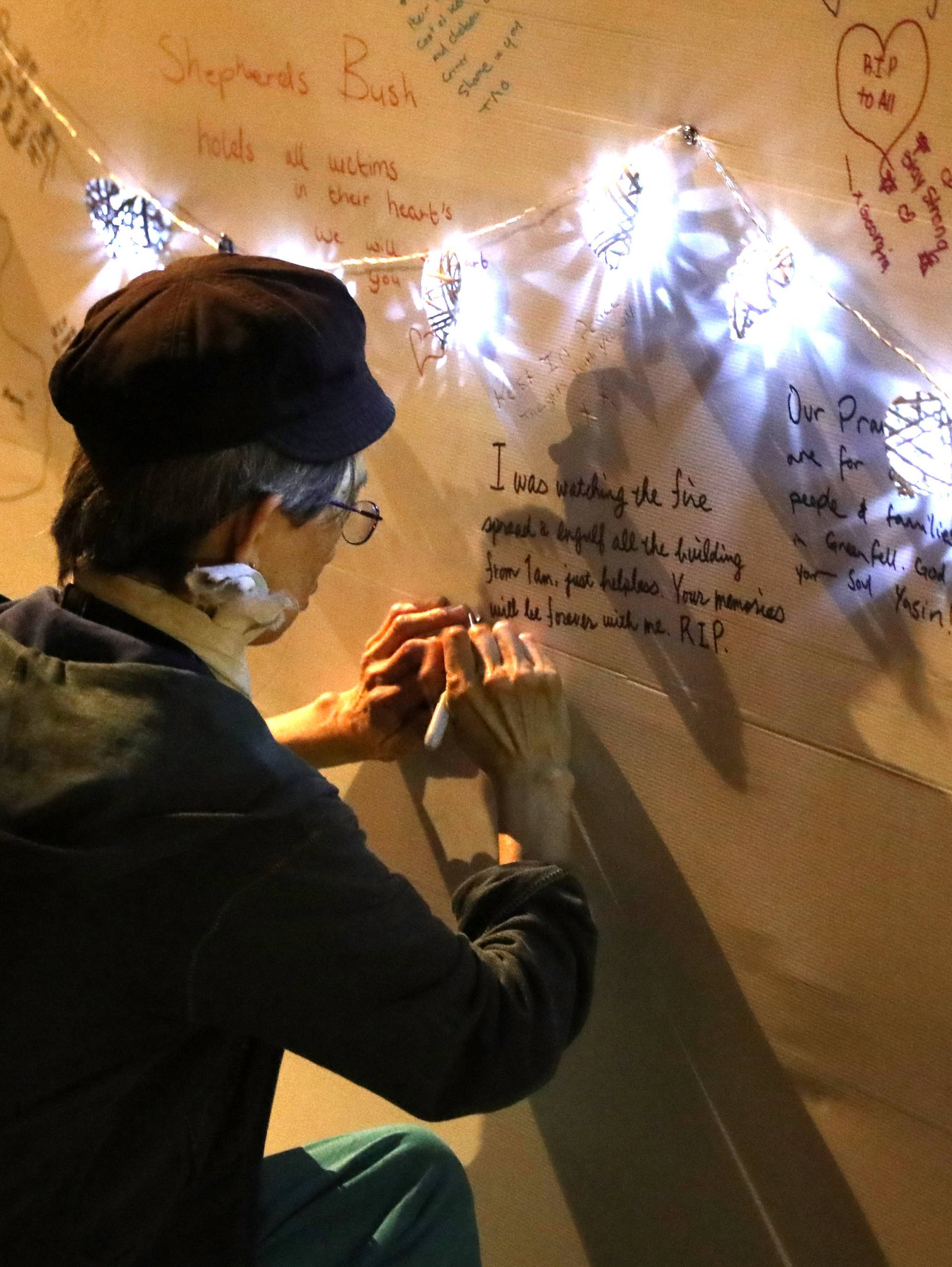 A woman writes a message of condolence on a wall  near a tower block severely damaged by a serious fire, in north Kensington, West London